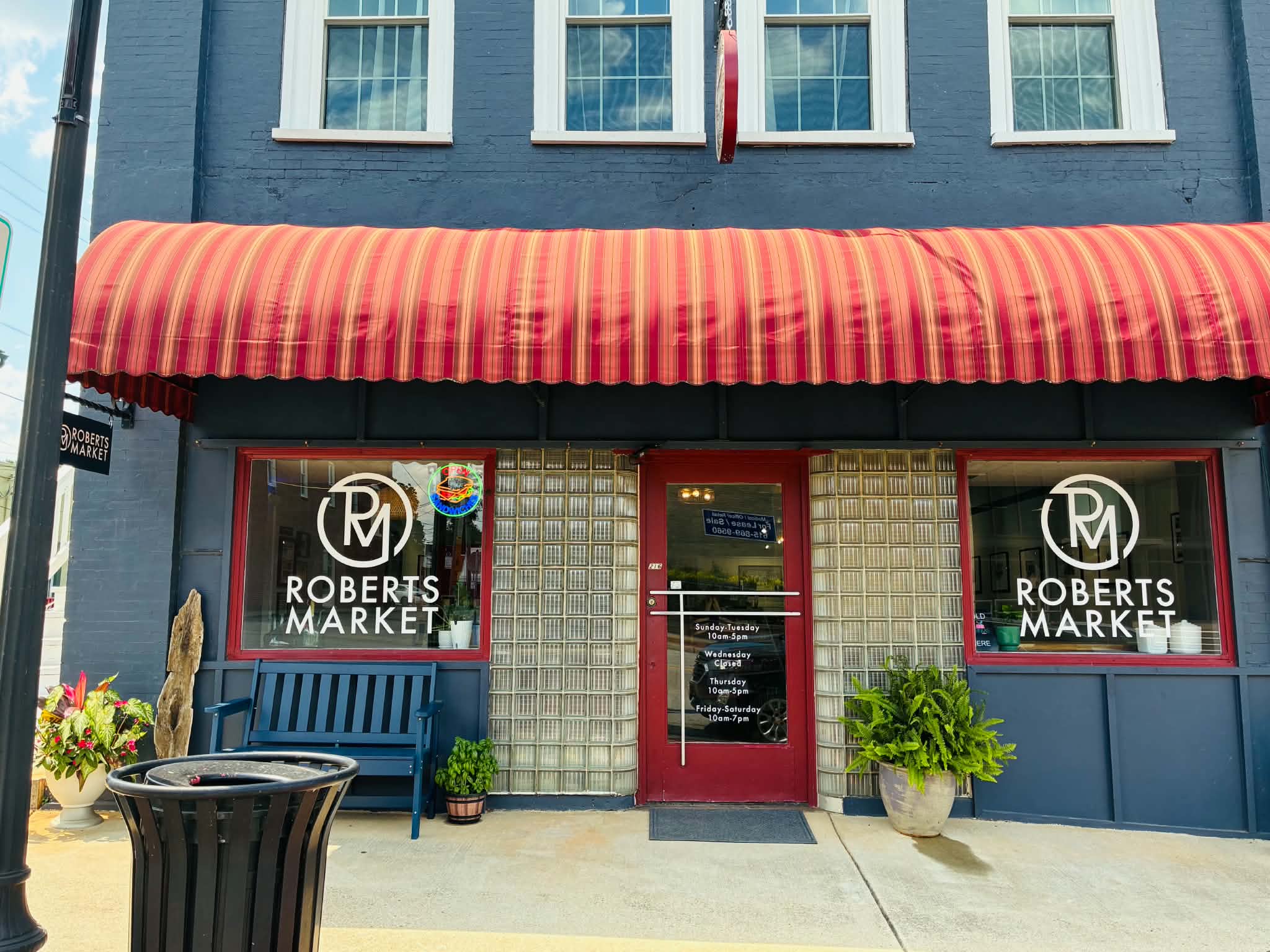 Roberts Market navy brick storefront with red striped awning and store hours posted on the red door