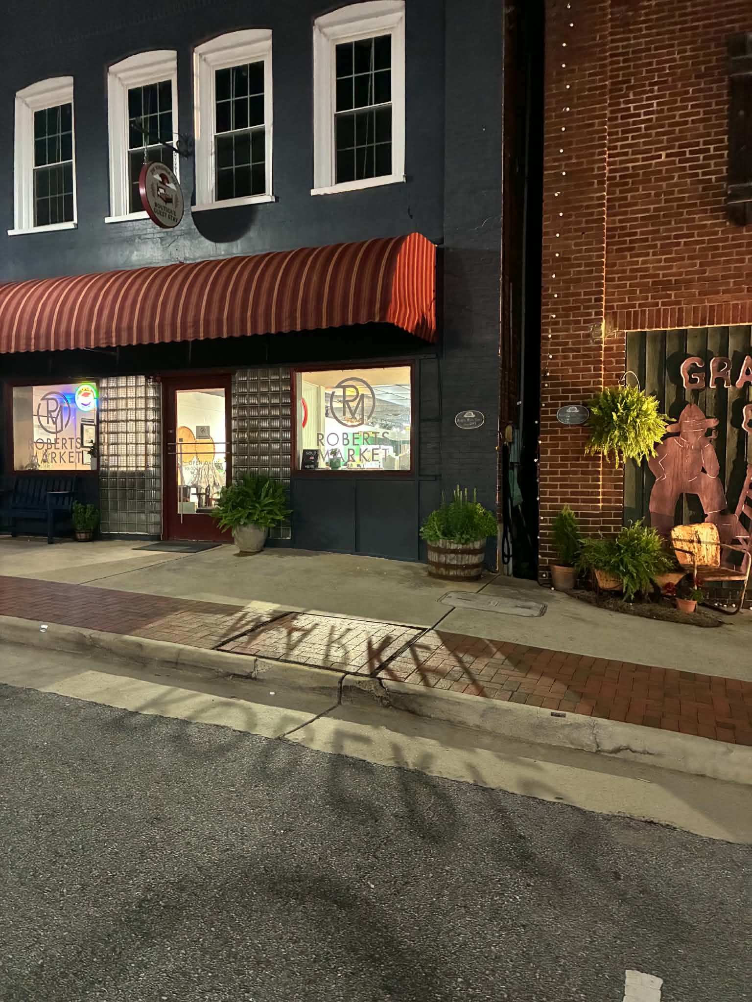Roberts Market storefront lit up at night with its red striped awning and glowing sandwich sign